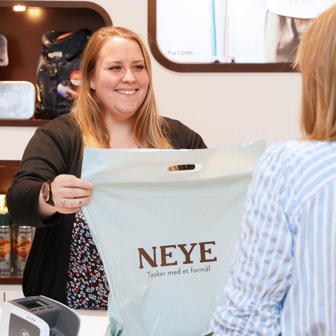 Medarbejder fra Neye i Randers giver kunde en pose med købte varer. 